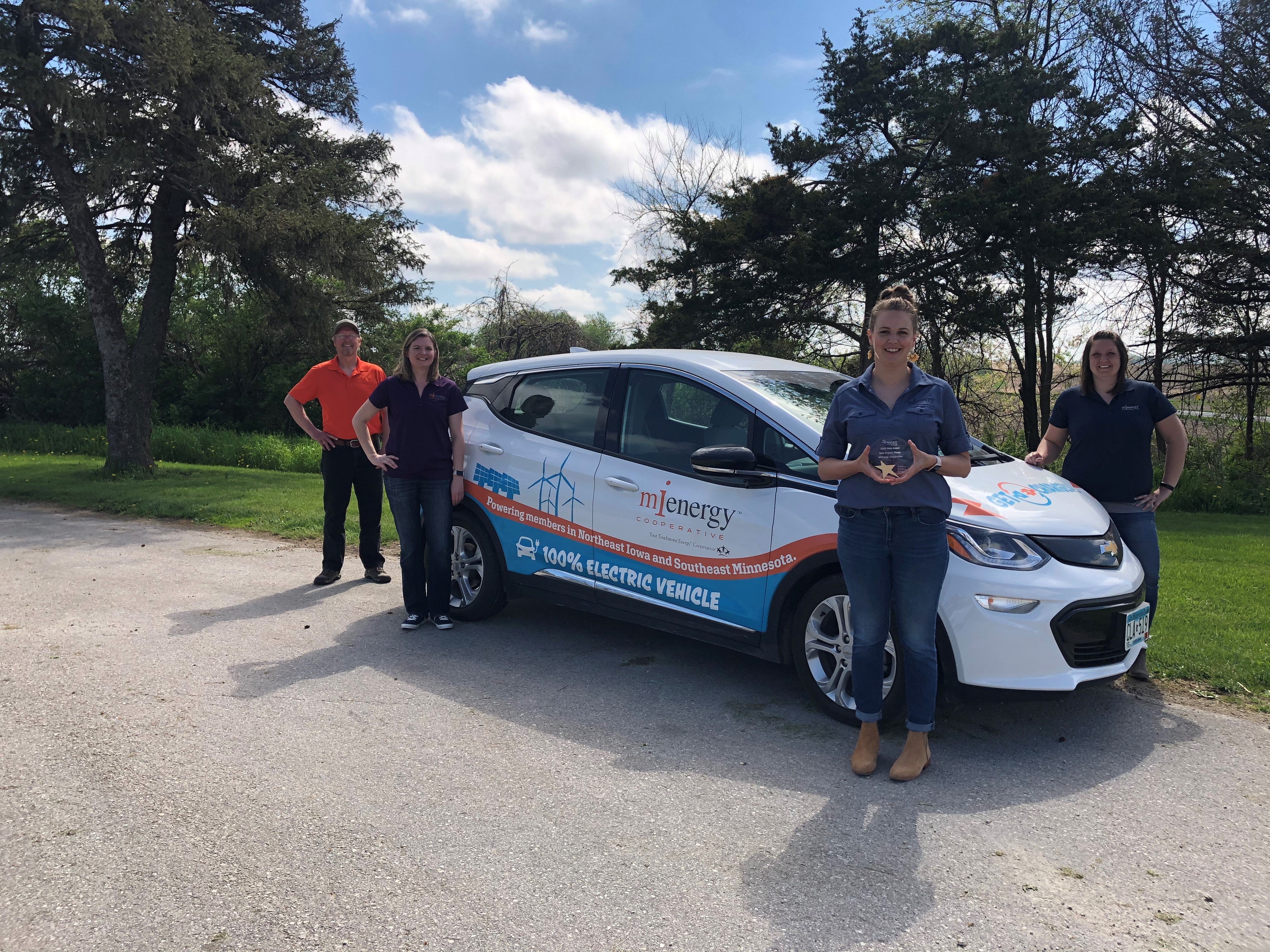 photo of employees standing in front of electric car holding award